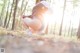 A woman crouching down in the woods with her back to the camera.