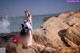 A woman in a bikini standing on a rock by the ocean.