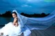 A woman in a wedding dress sitting on a dock.